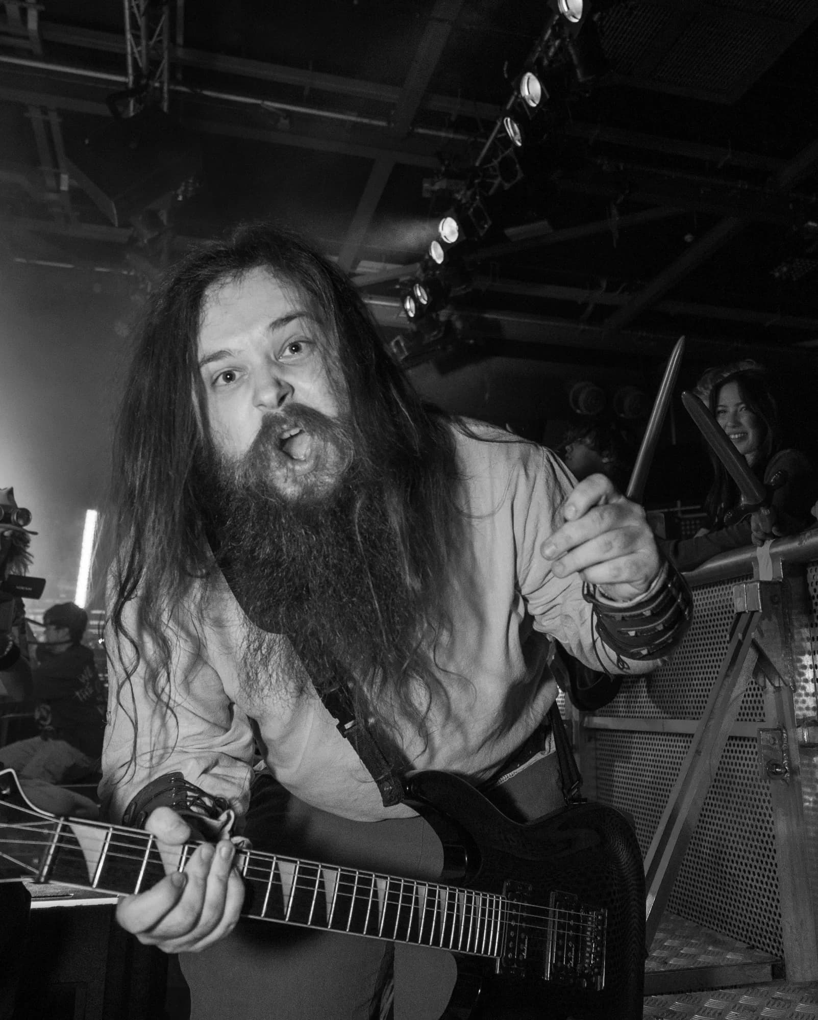 The guitarist leans out over the barrier into the crowd, mouth open mid-roar, caught in stark black and white under the stage lights.