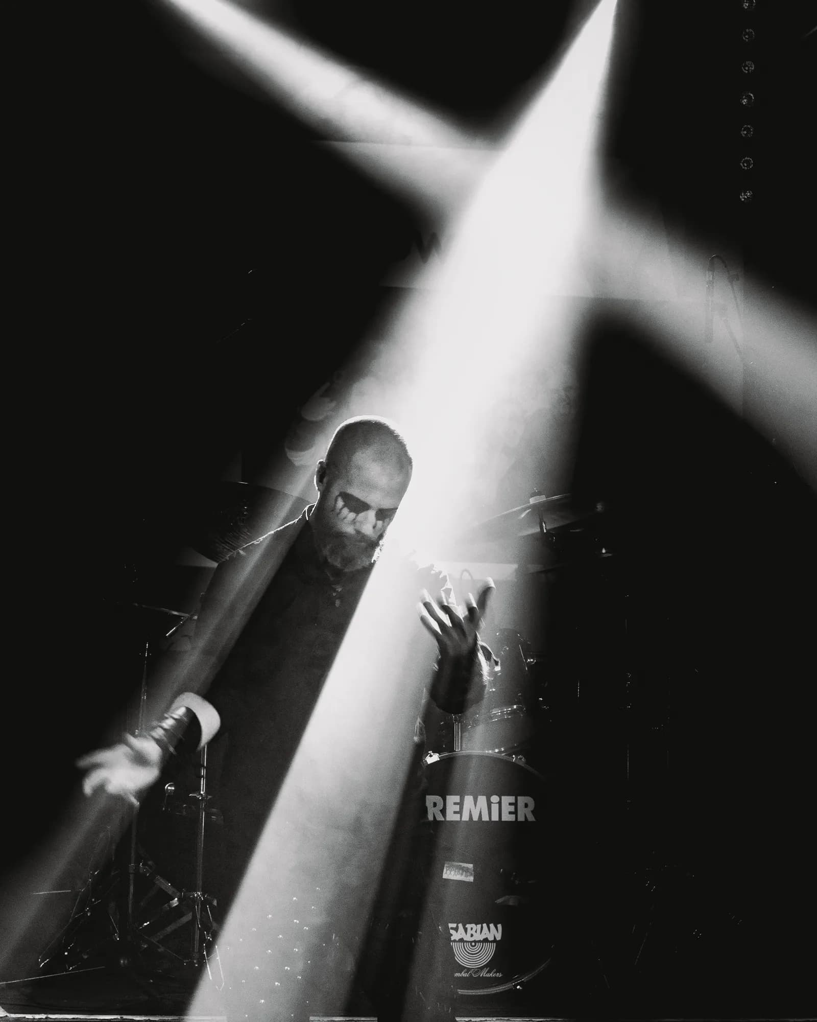 The vocalist crouches in a hard shaft of white light, corpse-paint streaking his face, the drum kit looming behind.