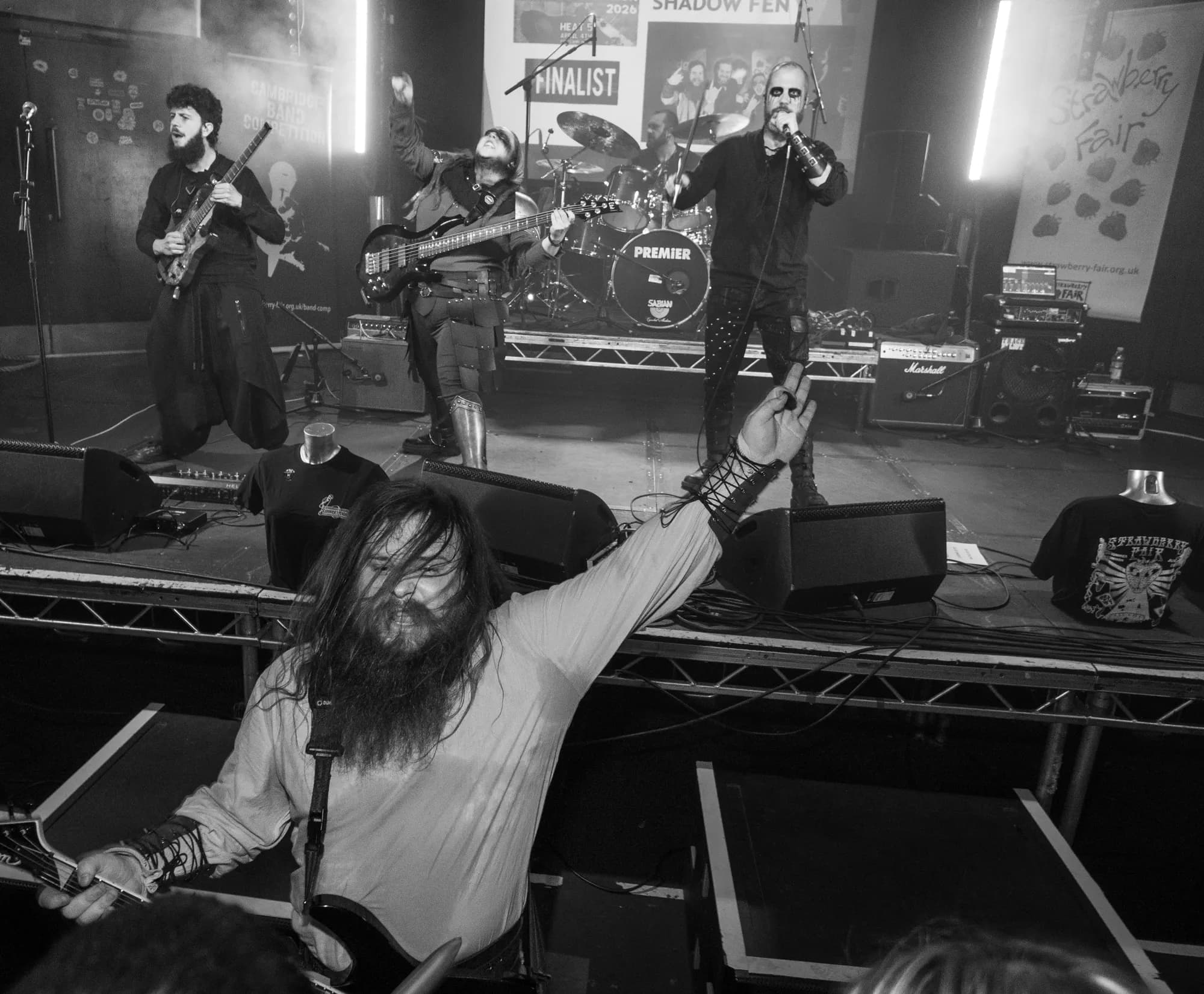 The vocalist reaches down to a bandmate at the barrier, the full band mid-set under the competition banner in black and white.
