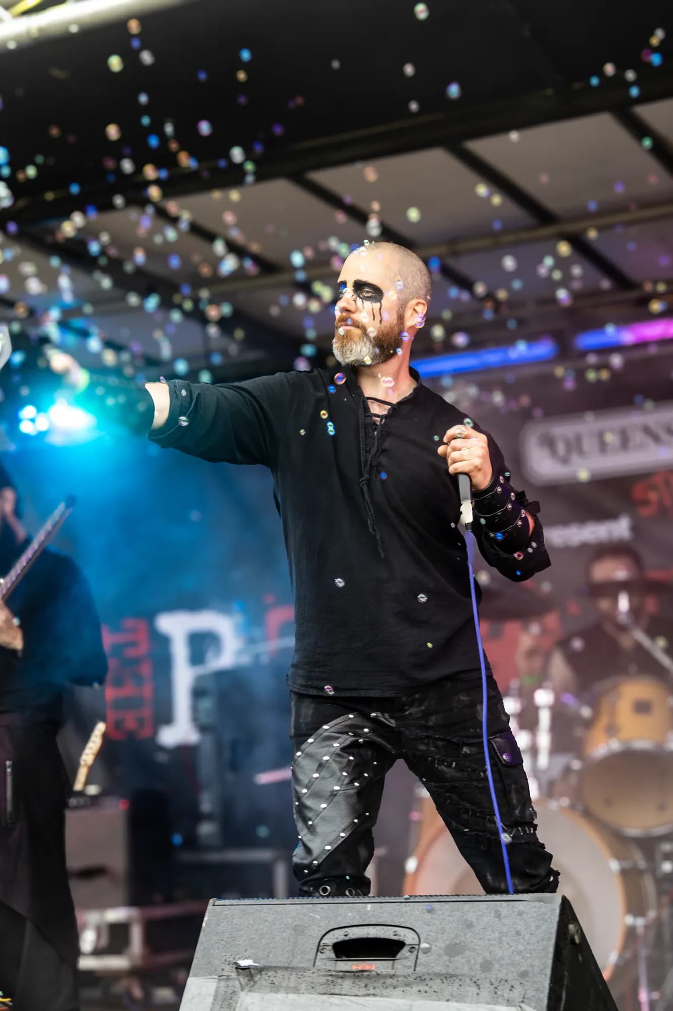 The vocalist reaches out from a festival stage, soap bubbles drifting through the daylight around him.